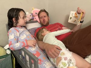 dad reading to two daughters in bed